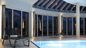 Piscina interna com espreguiçadeiras, grandes portas de vidro e claraboia.