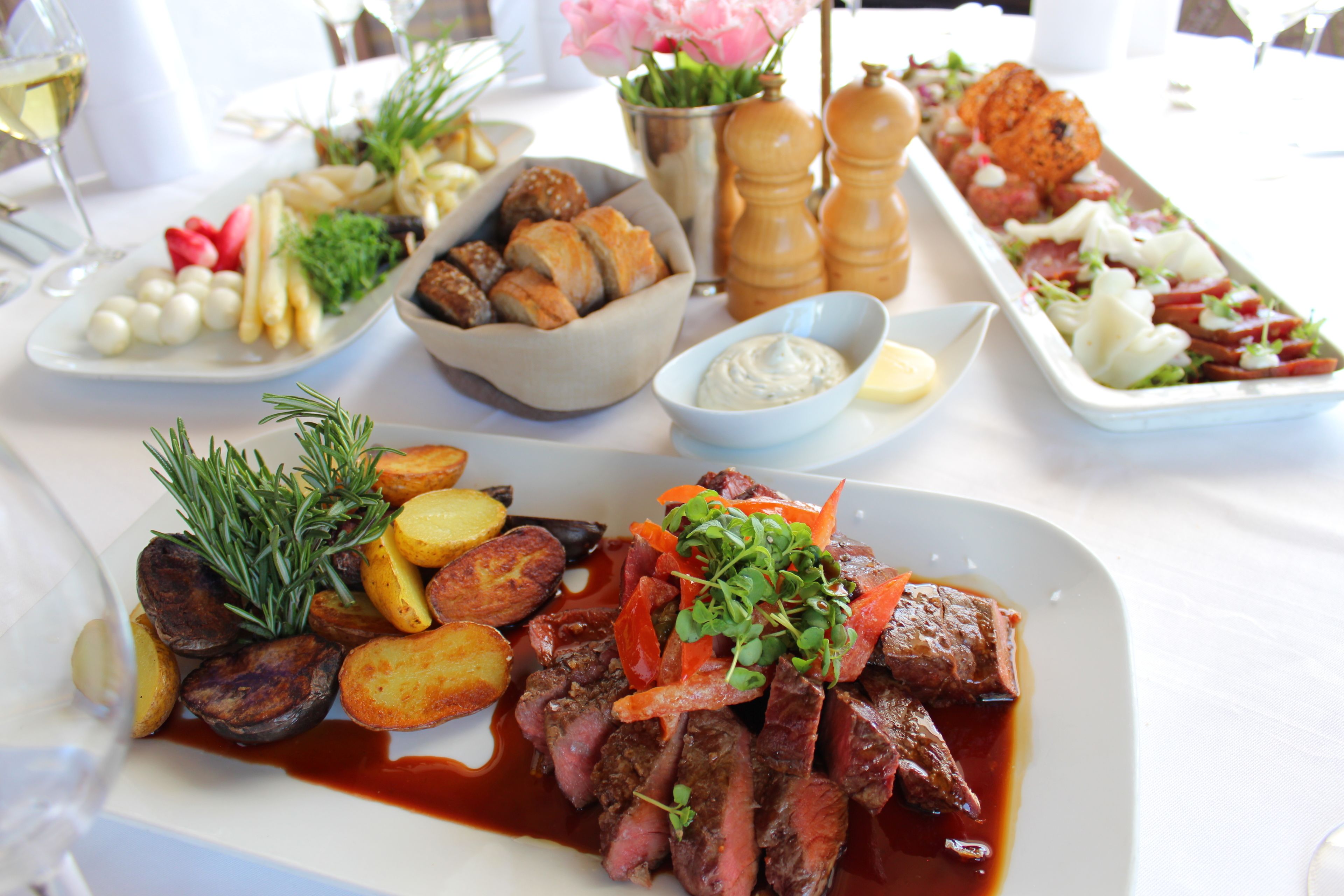 Verschiedene Gerichte auf einem Tisch, darunter ein Steak, Bratkartoffeln und Gemüse.