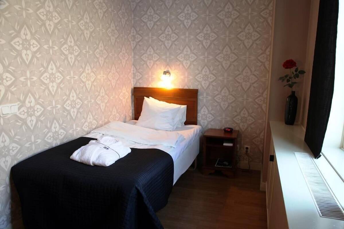 Ein ordentlich bezogenes Bett mit weißen Leinen, ein Nachttisch mit Lampe und ein an der Wand montierter Fernseher.