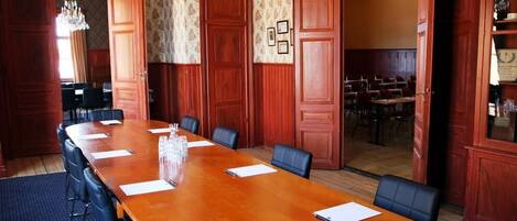 Un salón de conferencias con una larga mesa de madera, sillas negras y un candelabro.