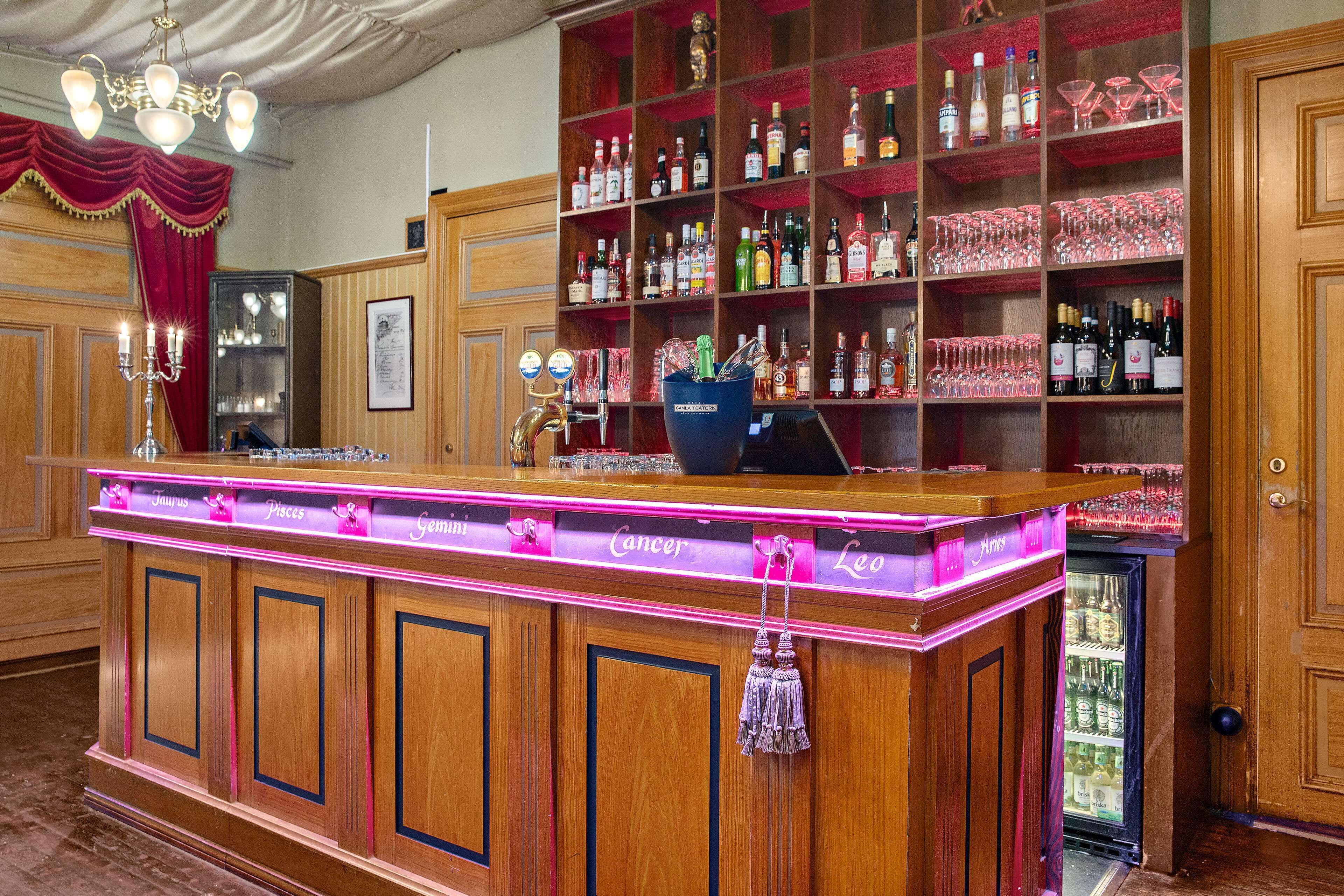 A bar area with wooden cabinets, shelves with bottles and glasses, and a neon-lit bar counter.