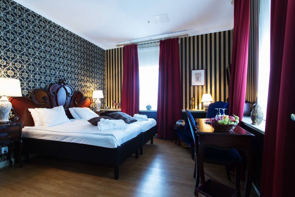 Ein Hotelzimmer mit einem großen Bett, einem Schreibtisch mit Stuhl, einem Fenster mit Vorhängen und einer Wand mit Muster.