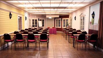 Un salón de conferencias con filas de mesas y sillas, un escenario y una puerta que da a otra sala.