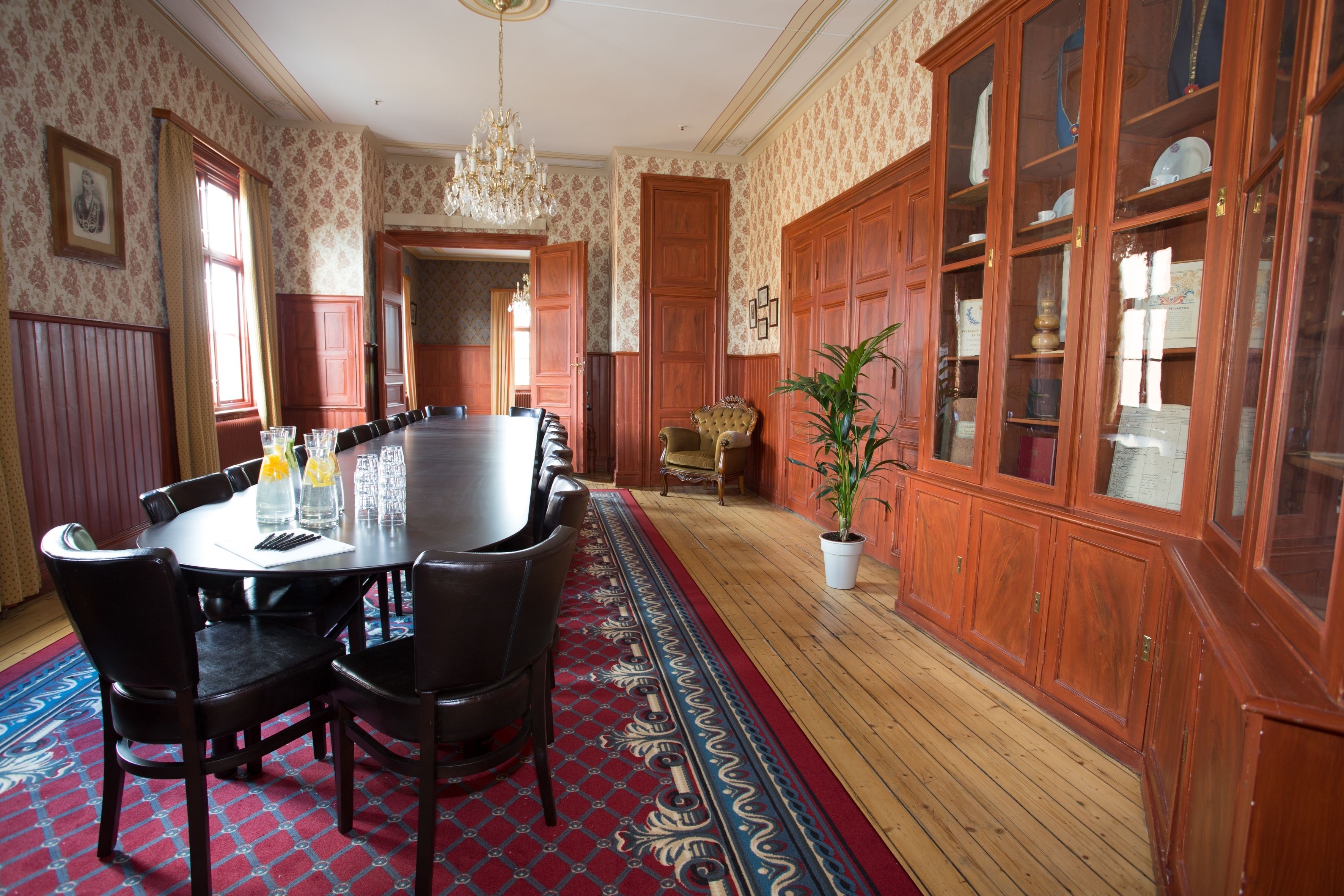 Une salle à manger élégante, avec une grande table ronde, des chaises en bois et un tapis rouge à motifs.
