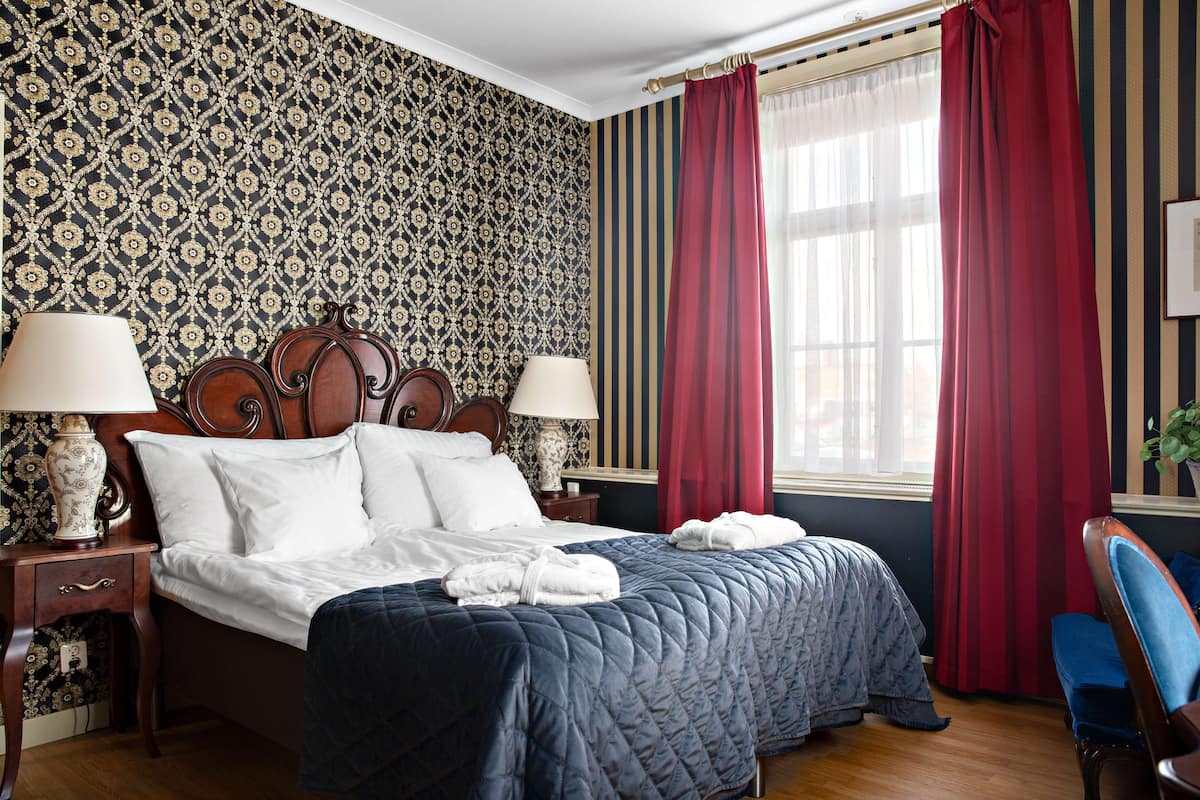 Ein Hotelzimmer mit einem großen Bett, zwei Nachttischen mit Lampen, einem roten und weißen Streifenvorhang und einem strukturierten Wandbild.