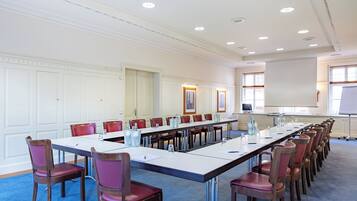 Ein Konferenzraum mit einem langen Tisch, roten Stühlen und einer Whiteboard-Tafel.