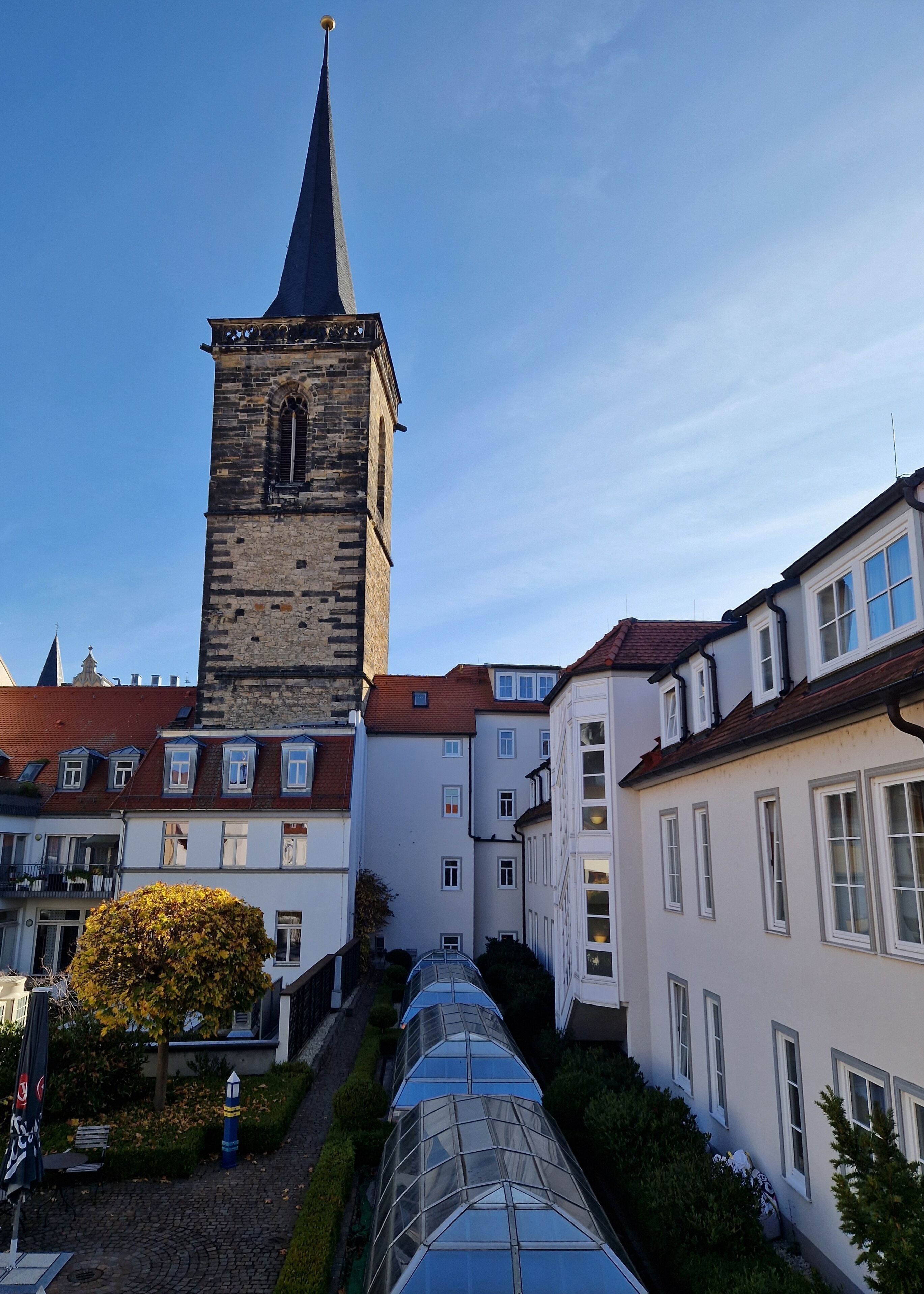 A historic tower with a pointed spire, surrounded by traditional buildings with white facades and red-tiled roofs.