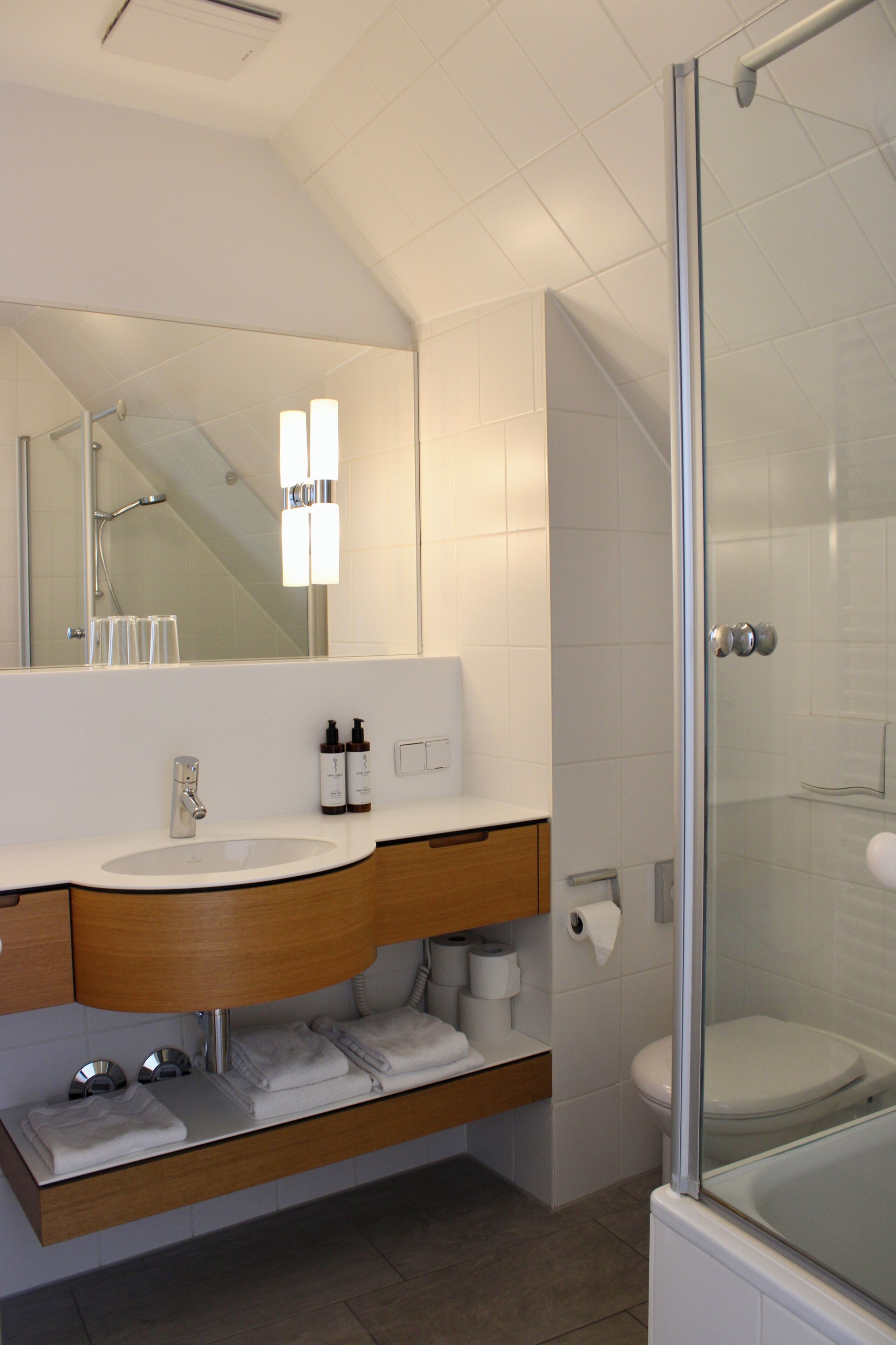 Une salle de bain moderne avec une douche à parois de verre, un lavabo blanc et un miroir au-dessus du meuble-lavabo.