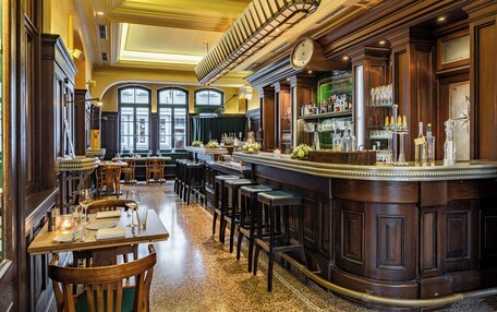 A bar area with wooden bar stools, a counter with bottles and glasses, and a clock on the wall.