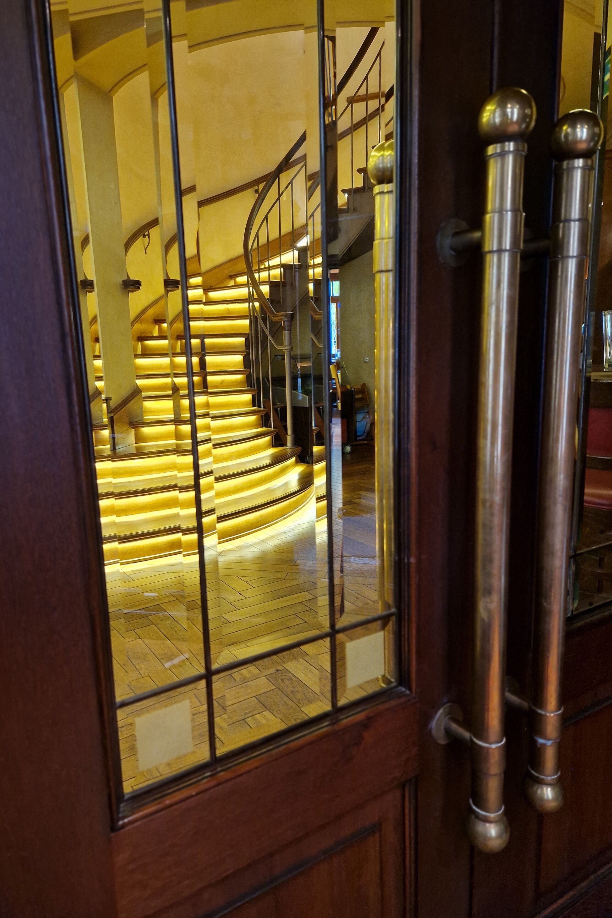 Eine Holztür mit Fensterglas, das eine Treppe mit Metallgeländer und Holzboden reflektiert.