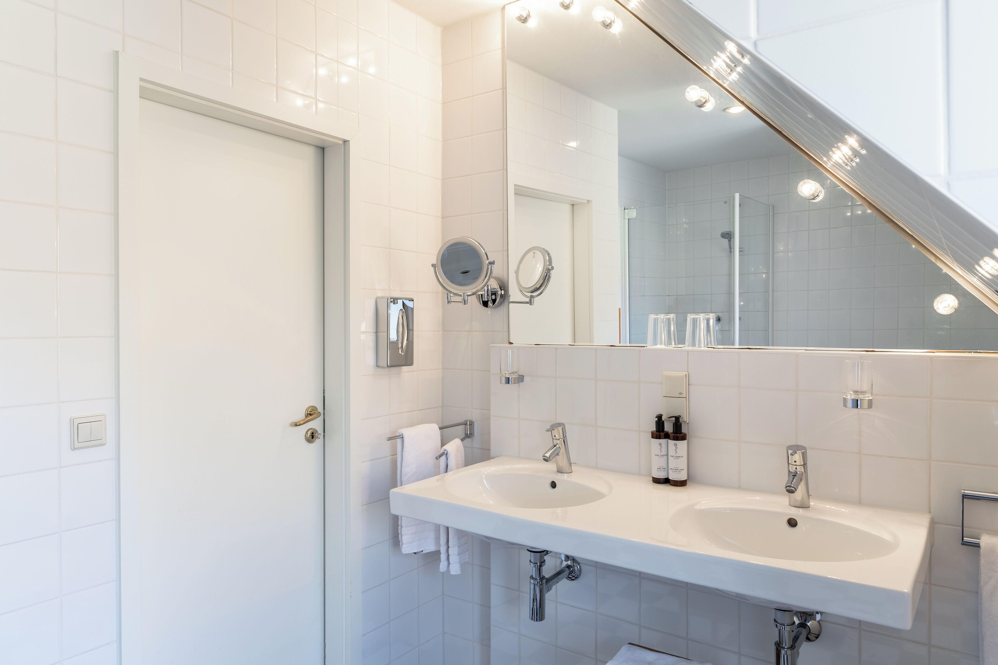 A modern bathroom with two sinks, a large mirror, and a shower area.