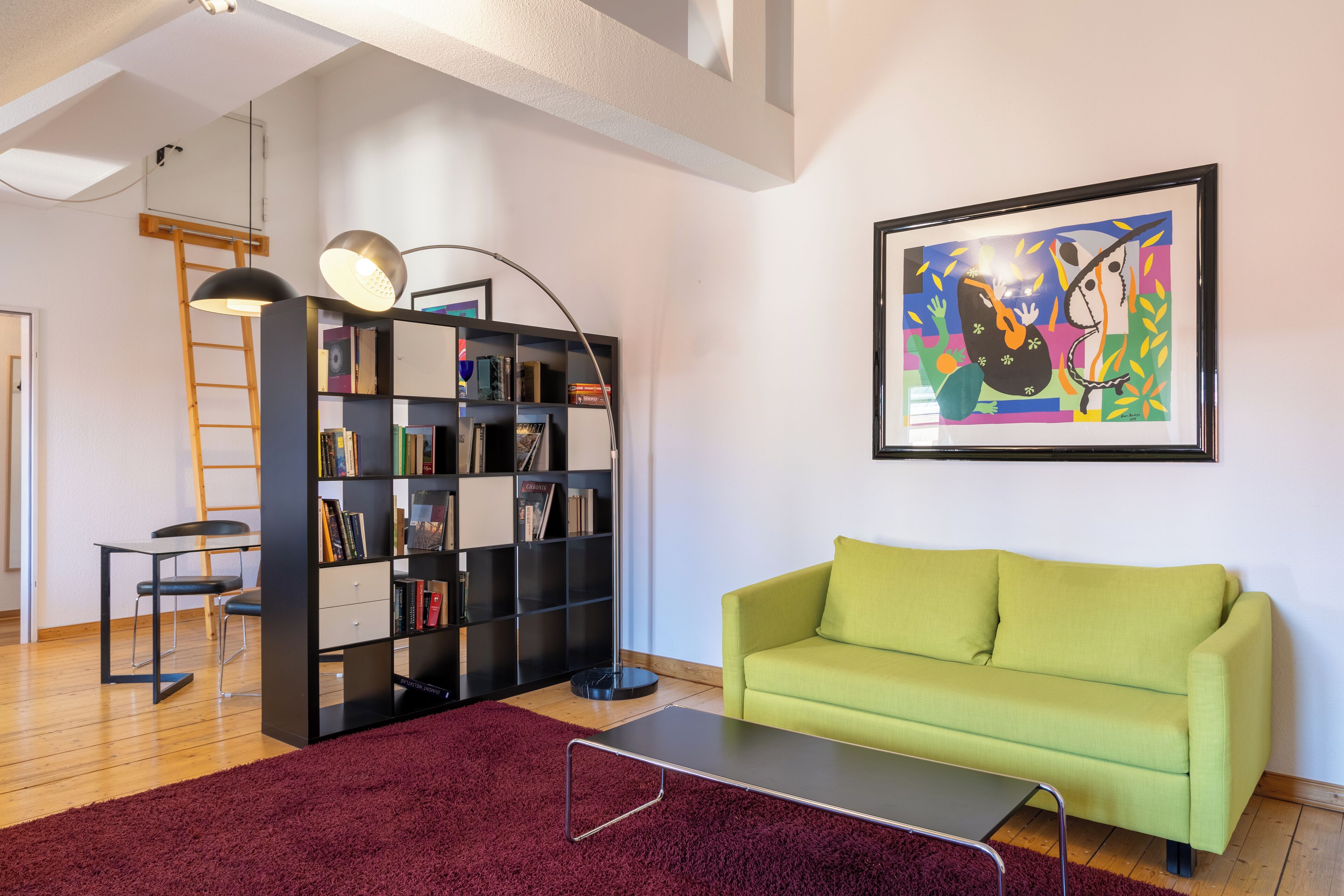 A living room with a green sofa, a black bookshelf, a red rug, and a framed abstract painting on the wall.