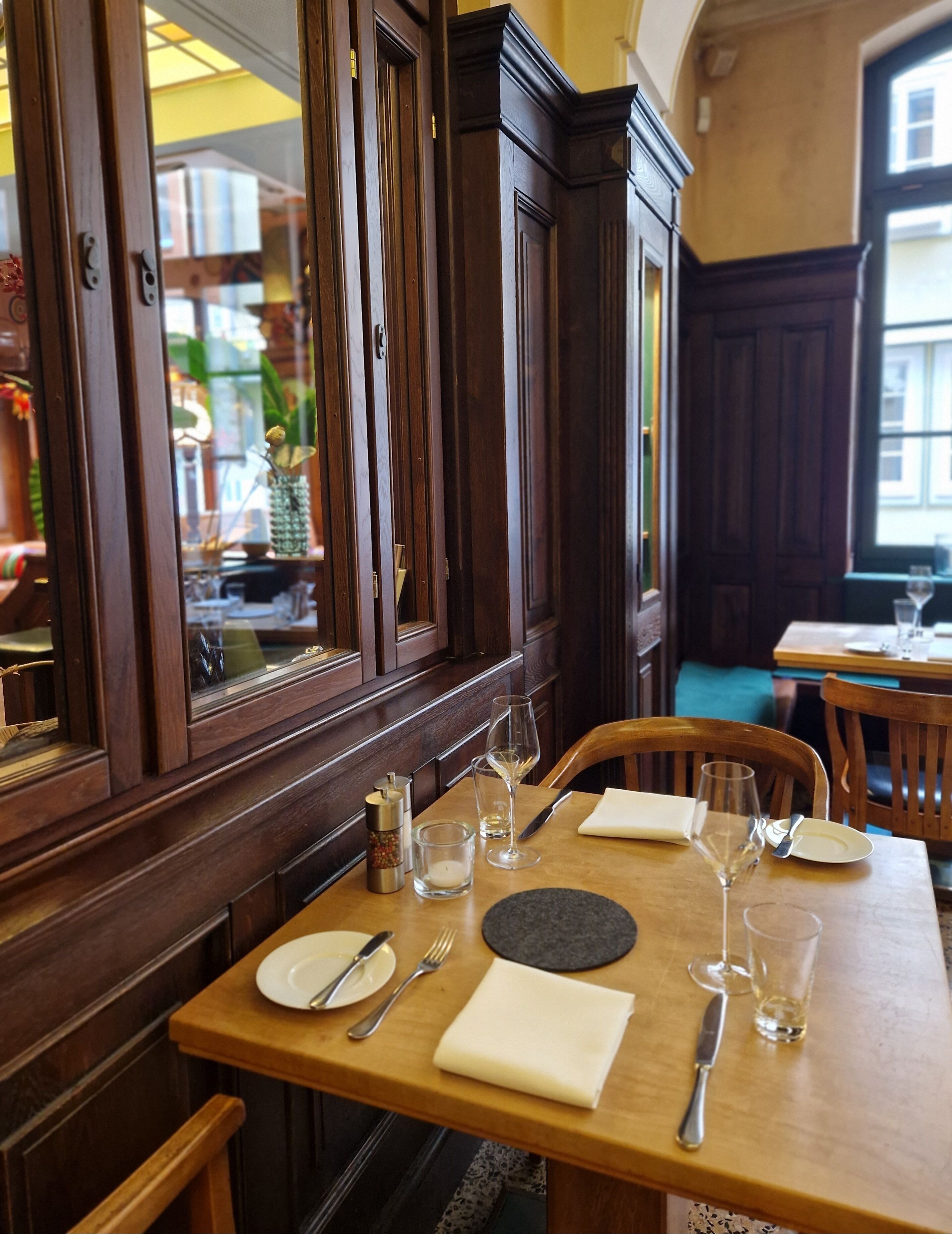 A dining table set with plates, cutlery, and glasses, with a window and wooden paneling in the background.