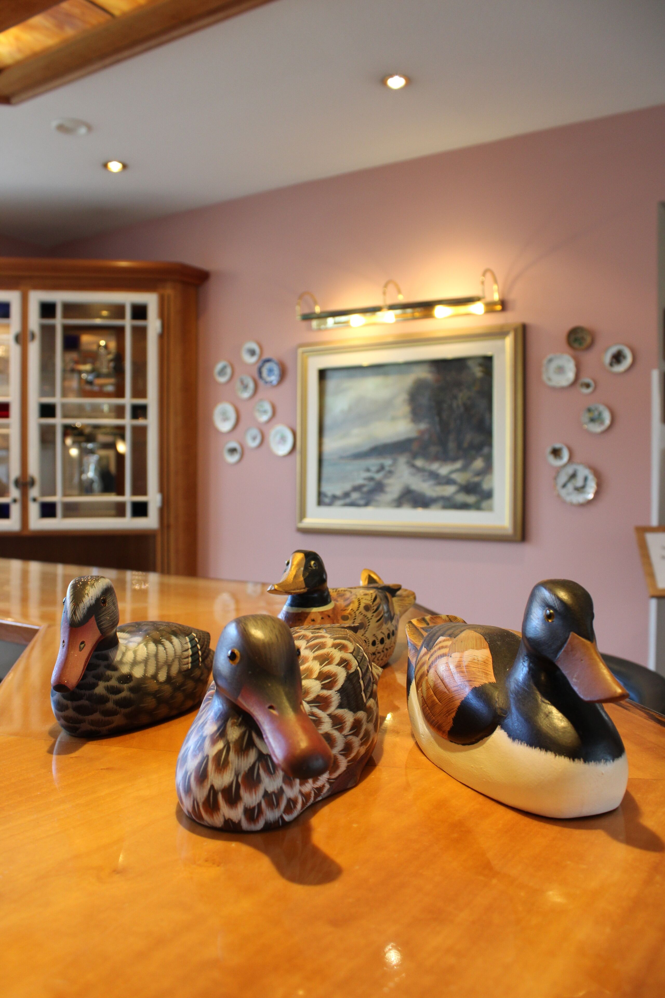 A table with three duck figurines and a framed painting on the wall.