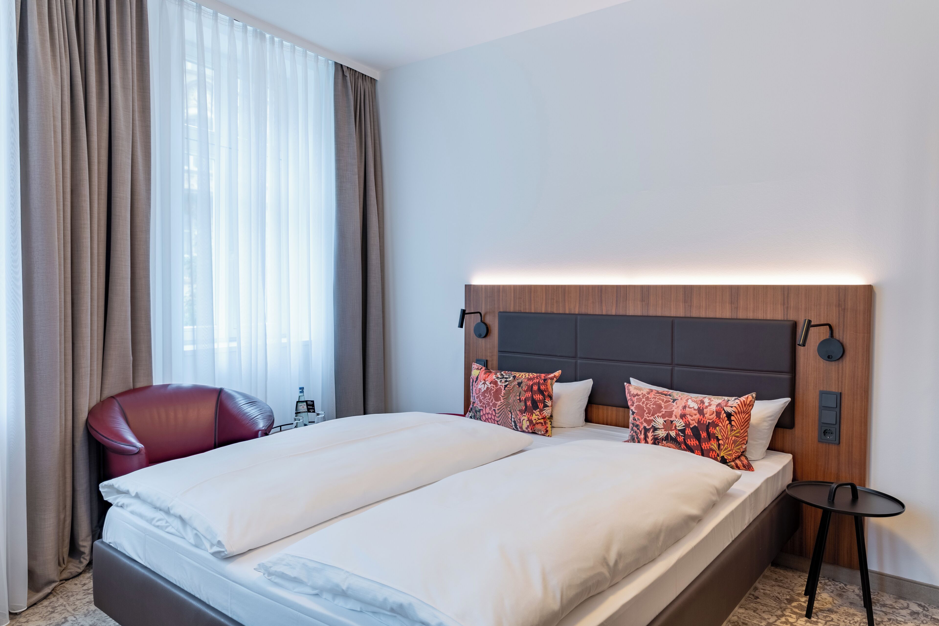 Une chambre d’hôtel avec un grand lit, un fauteuil en cuir rouge, une petite table et une table de chevet avec une lampe.
