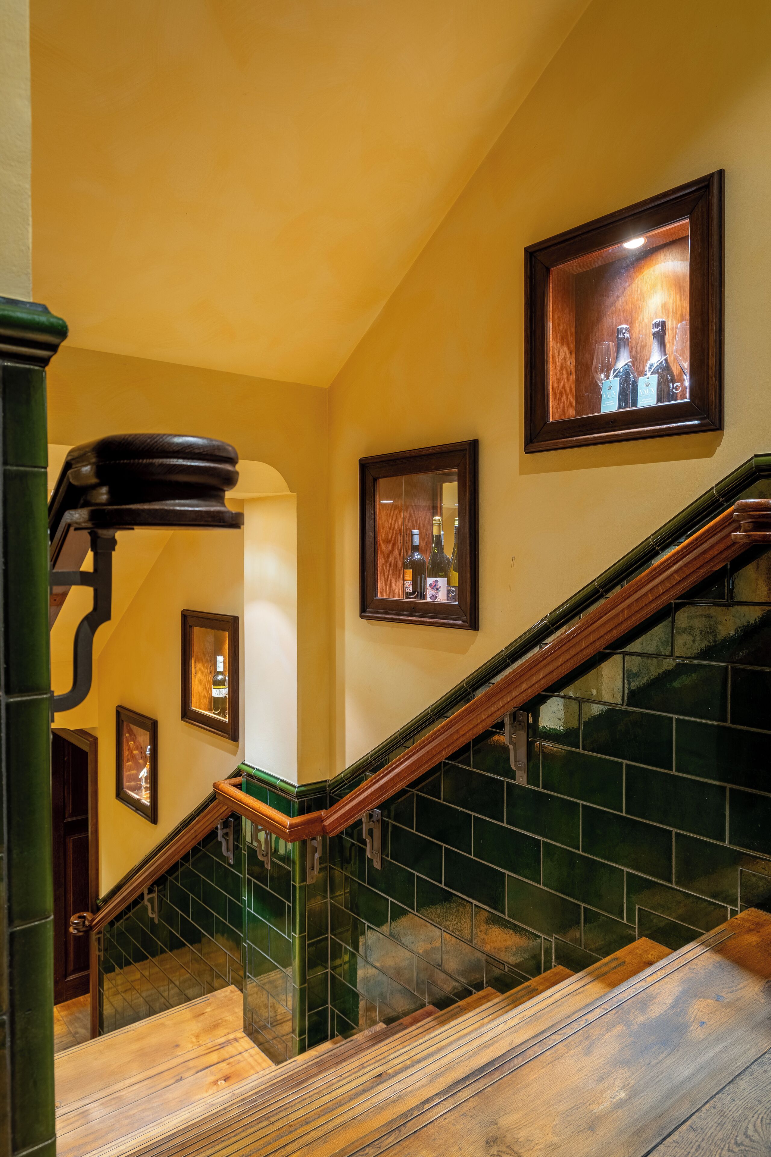 Un escalier dont les murs sont recouverts de carreaux verts et les marches sont en bois.