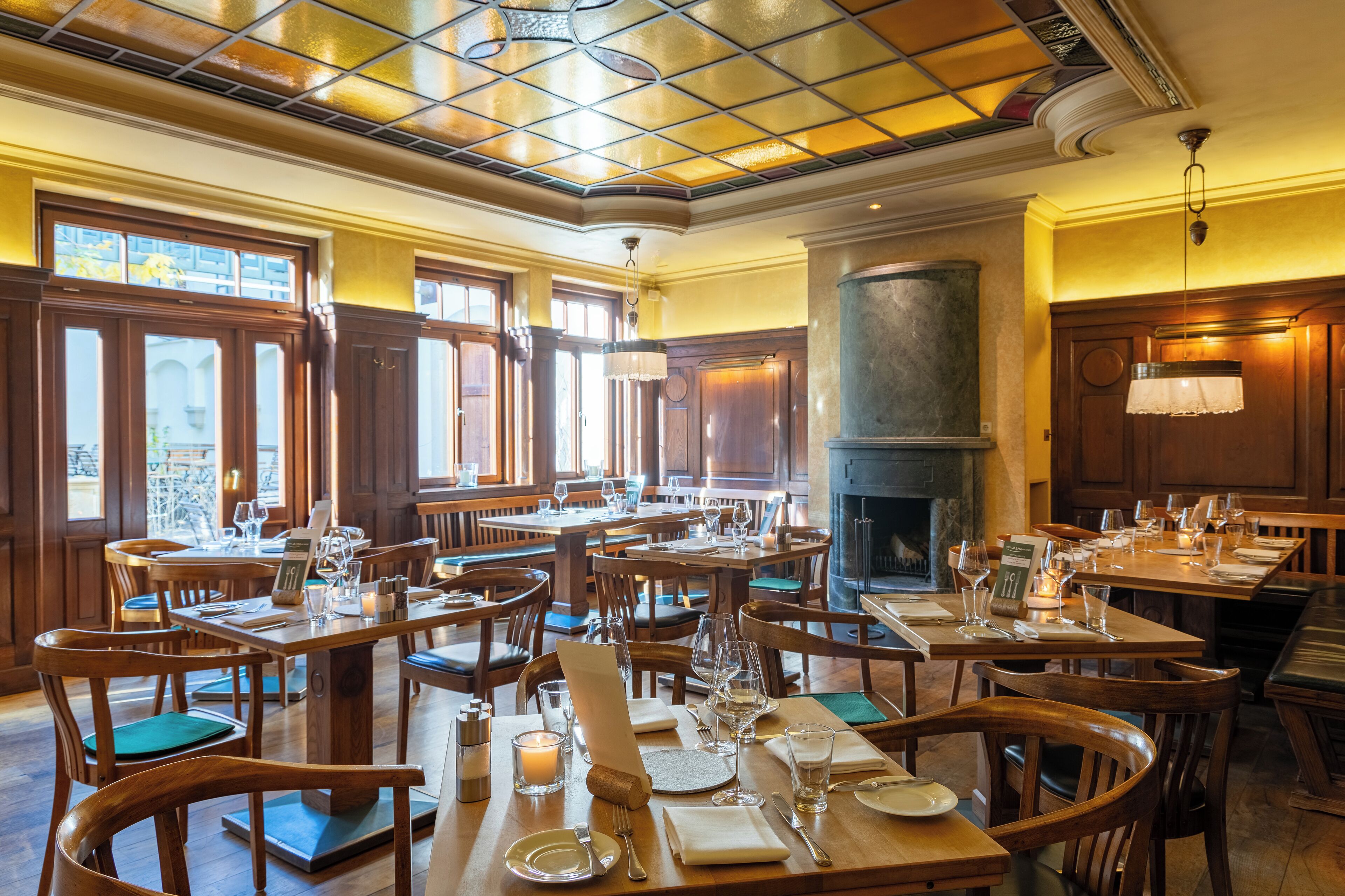A restaurant with wooden tables and chairs, a fireplace, and large windows.