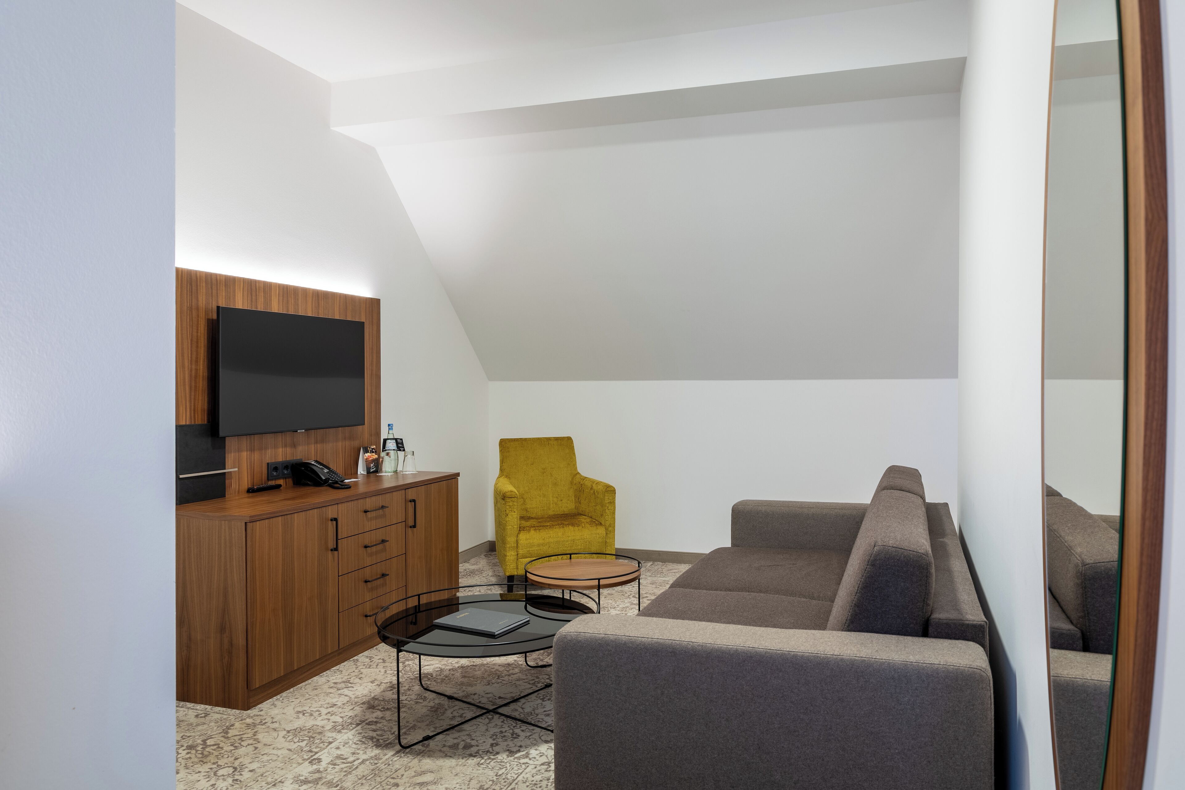 A modern living room with a flat-screen TV, wooden cabinet, yellow armchair, gray sofa, and a small round coffee table.
