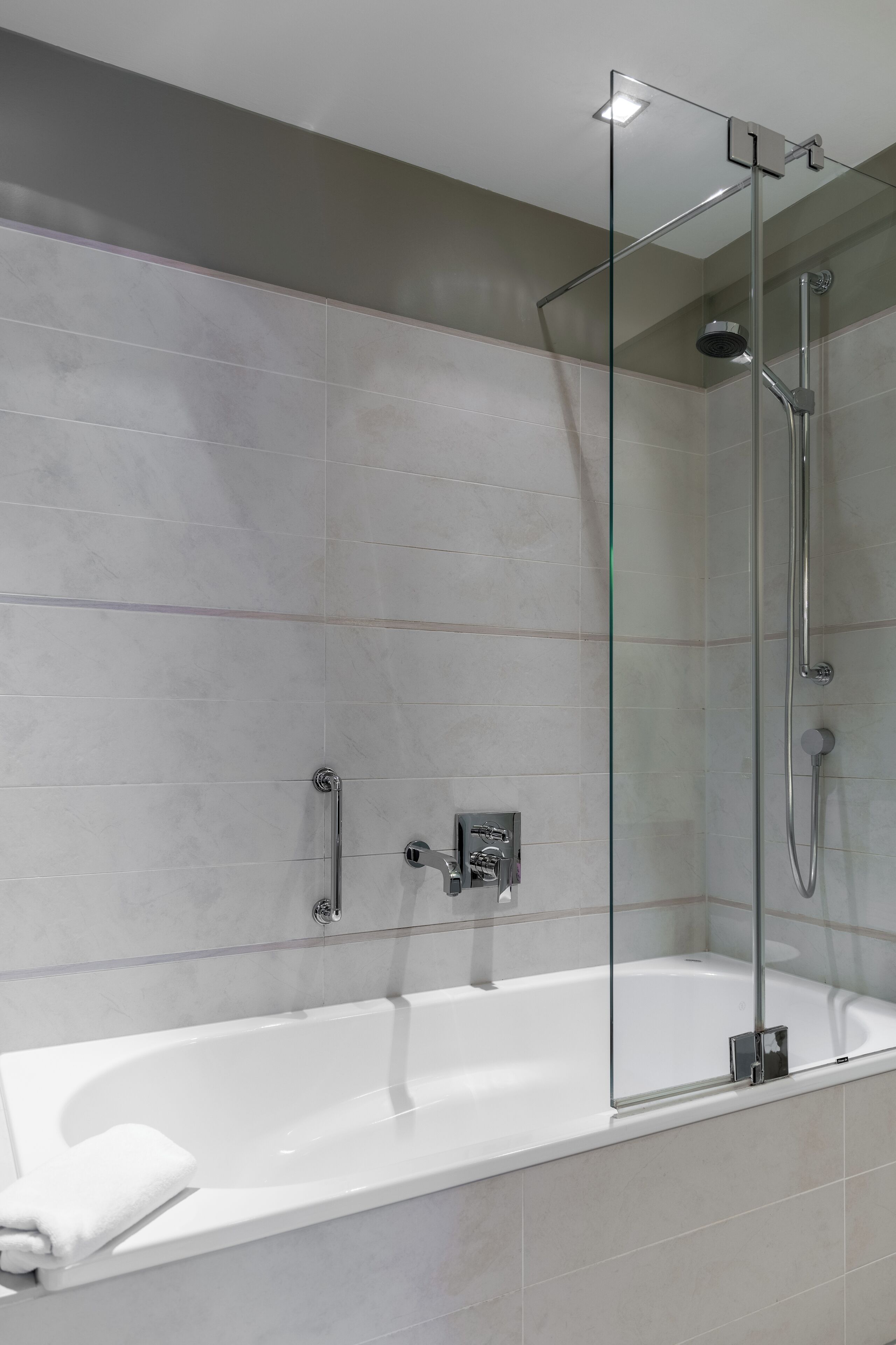Un bagno moderno con doccia vetro, vasca freestanding e soffione a mano.