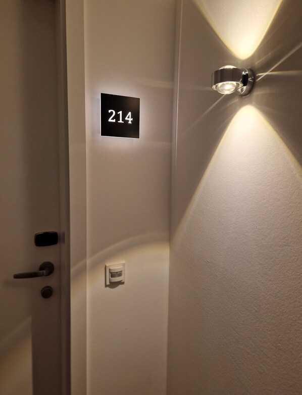 Una puerta con una placa que indica la habitación 214, un picaporte y una lámpara en la pared.