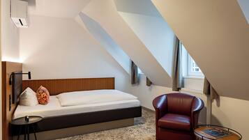 Une chambre d’hôtel moderne avec un lit, un fauteuil en cuir rouge, une petite table et une fenêtre avec des rideaux.