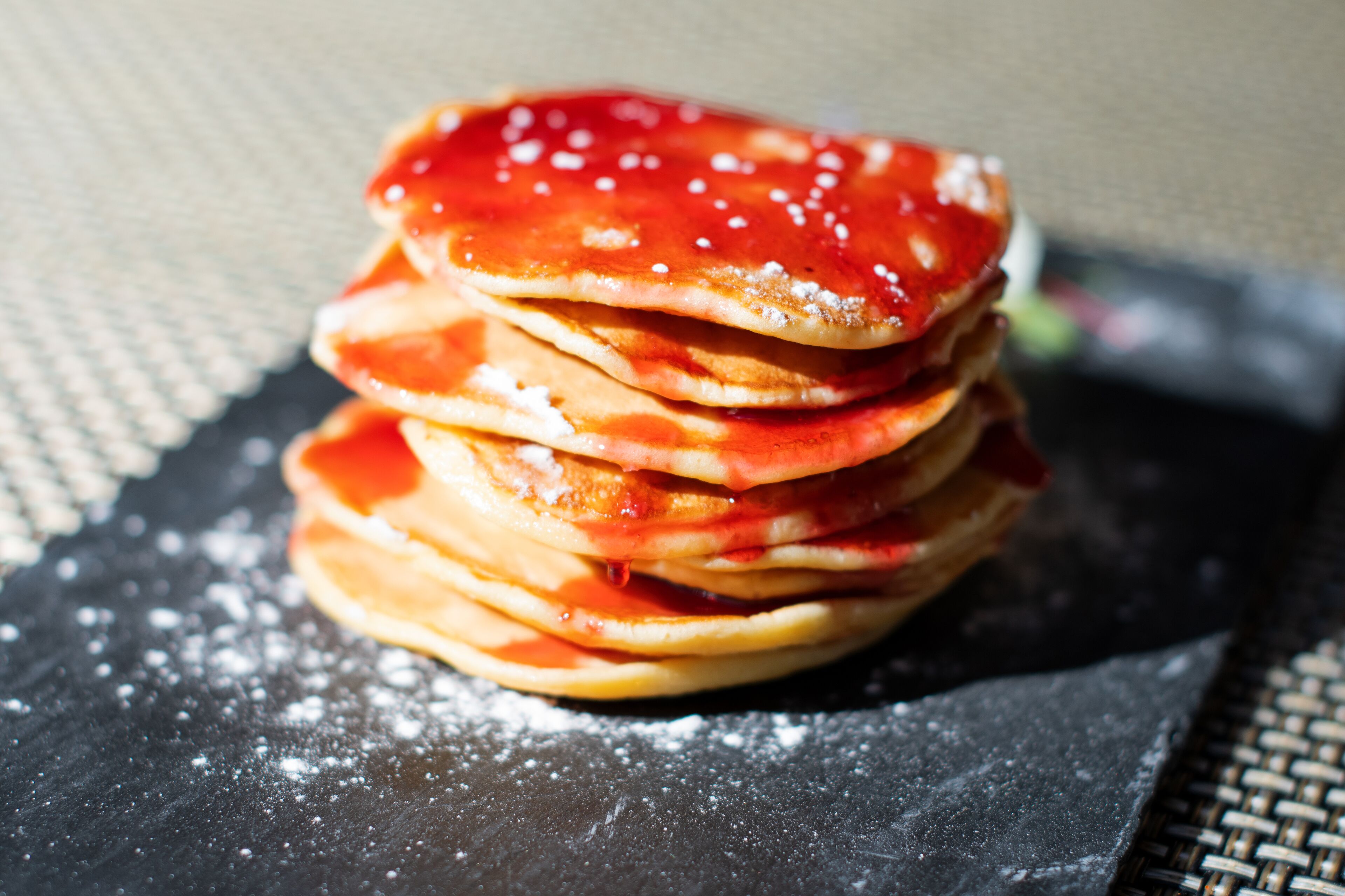 Ein Stapel Pfannkuchen mit rotem Sirup auf einer dunklen Unterlage.