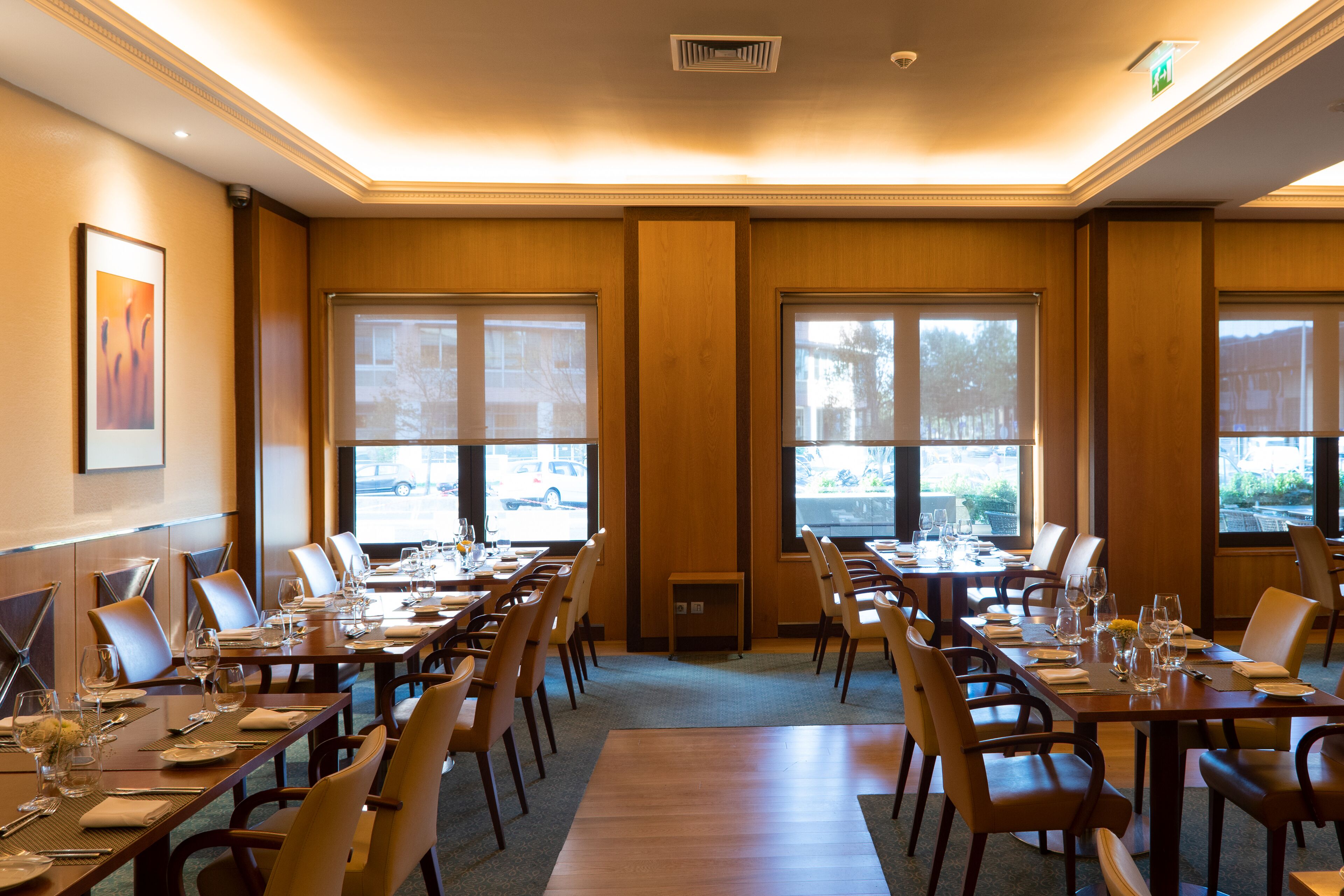 A conference room with multiple tables set for dining, large windows, and a view of the outside.