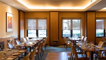 A conference room with multiple tables set for dining, large windows, and a view of the outside.