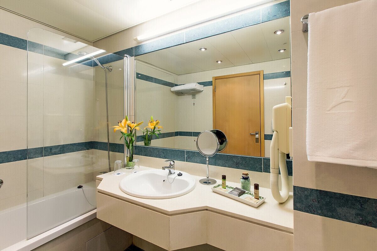 A bathroom with a glass shower enclosure, a sink with a mirror, and a towel hanging on the wall.