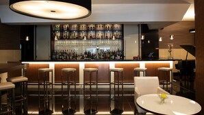 A modern bar area with a long counter, multiple stools, and a round table with a vase of flowers. - SANA Metropolitan Hotel (Lisbon)