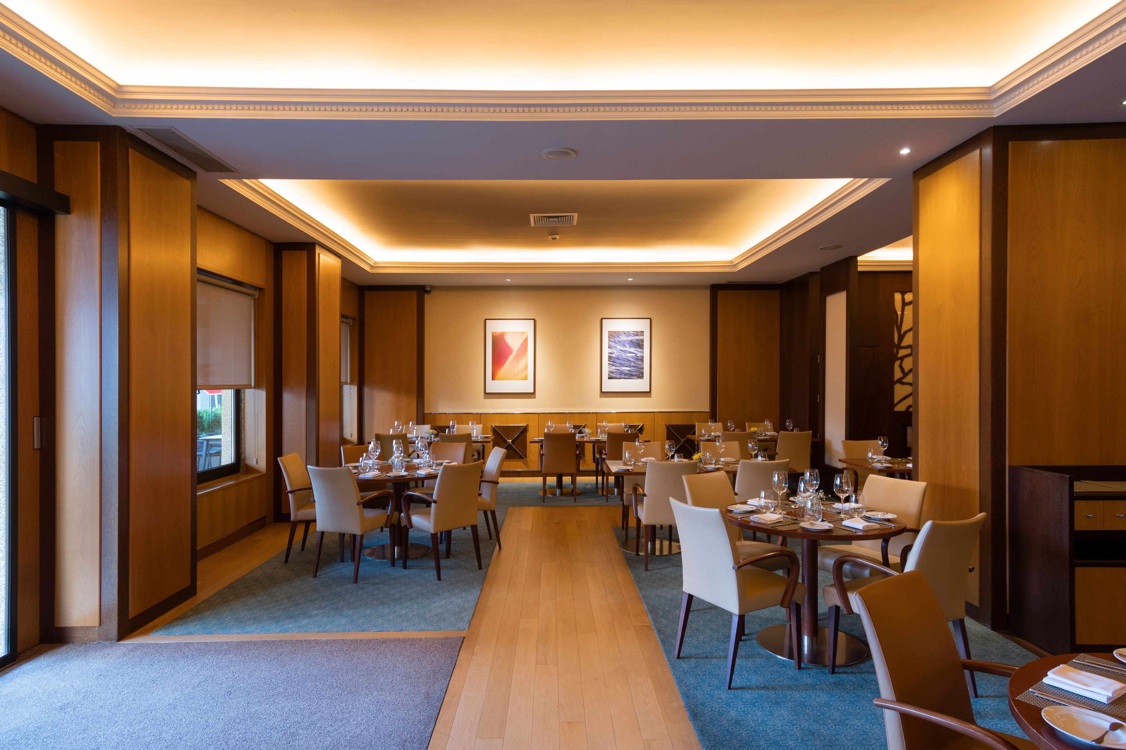 A hotel dining area with multiple tables and chairs, a central walkway, and framed artwork on the walls.