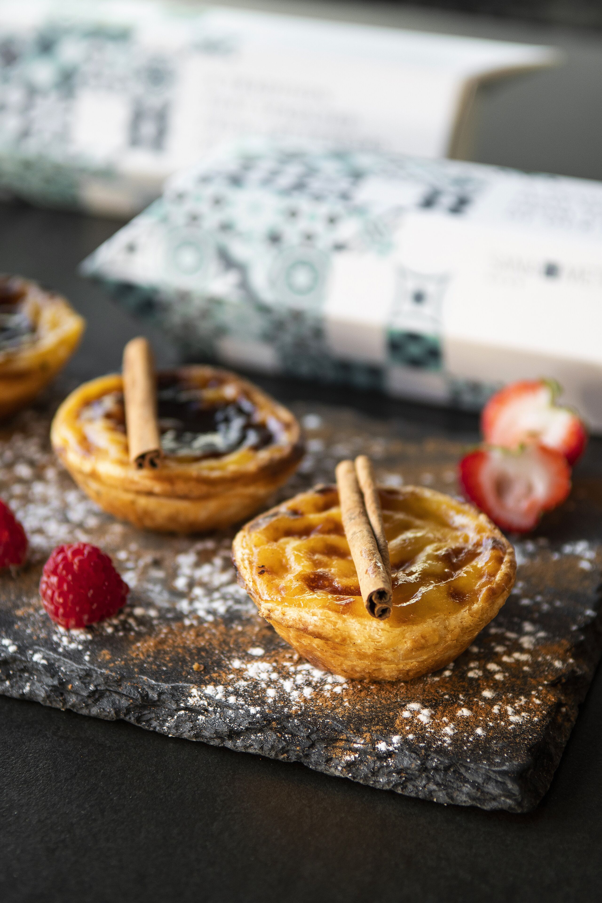 Three small pastries on a slate serving board, dusted with powdered sugar, with a cinnamon stick on each.