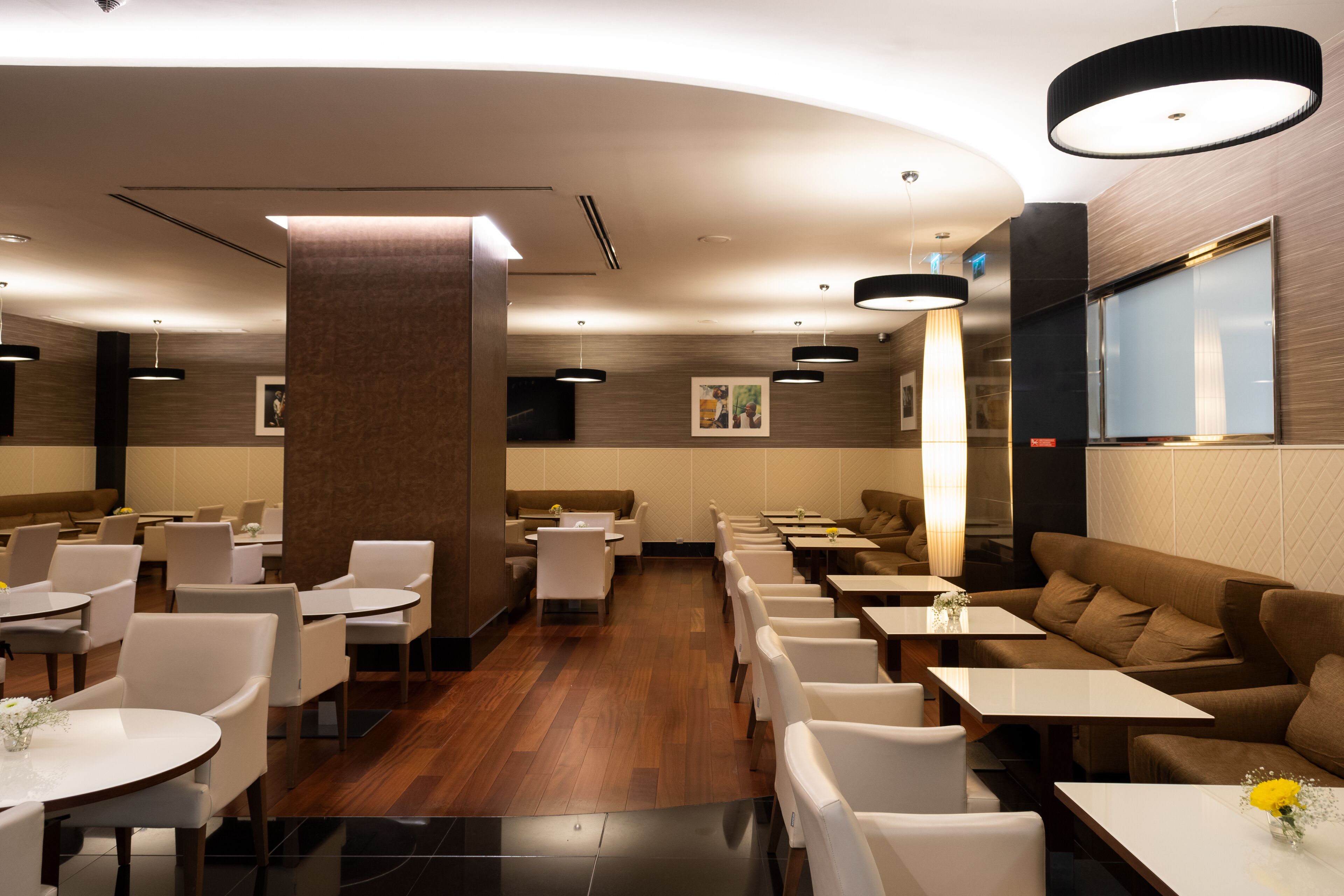 Een modern restaurant met diverse zitmogelijkheden, zoals zitjes en tafels, een houten vloer en moderne verlichtingsarmaturen.