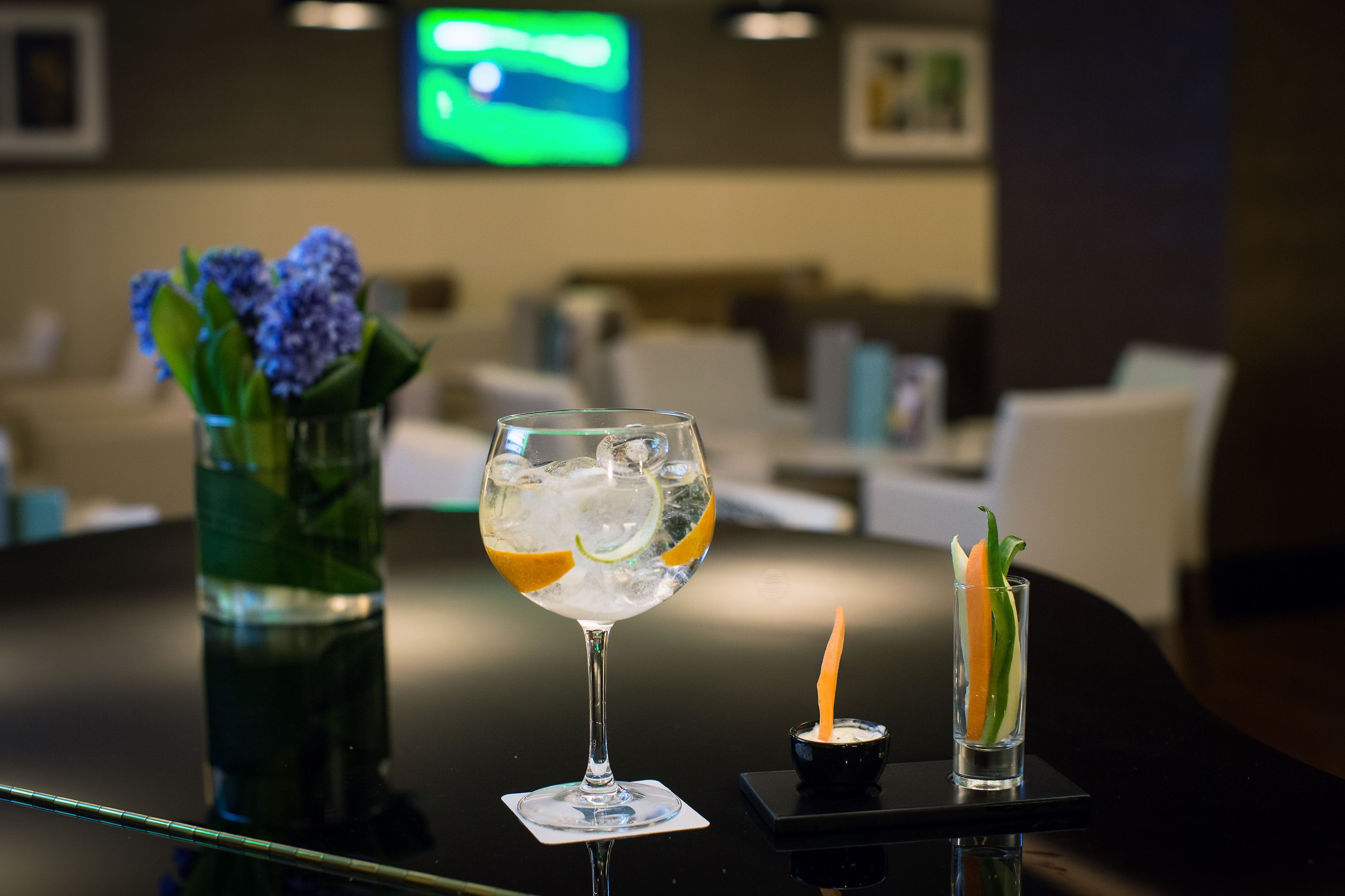 Zona de bar con un vaso de bebida helada, una vela pequeña y un jarrón con flores.