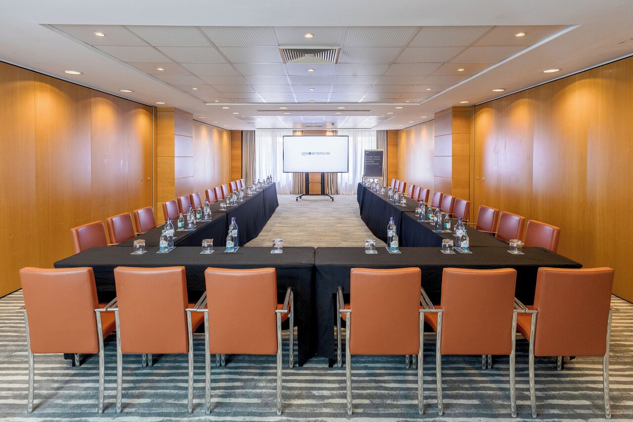 Un salón de conferencias con una larga mesa, sillas anaranjadas y una pantalla de proyector al frente.