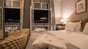 A hotel room with a bed, a bench, and a view of a cityscape at night. - Hotel Metropole (Lisbon)