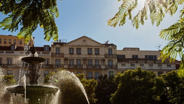 A fountain with water jets in a public square, surrounded by buildings with classical architecture. - Hotel Metropole (Lisbon)