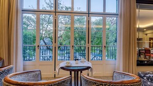 A dining area with a table set for two, surrounded by wicker chairs, large windows with a view of greenery, and a door leading outside. - Hotel Metropole (Lisbon)