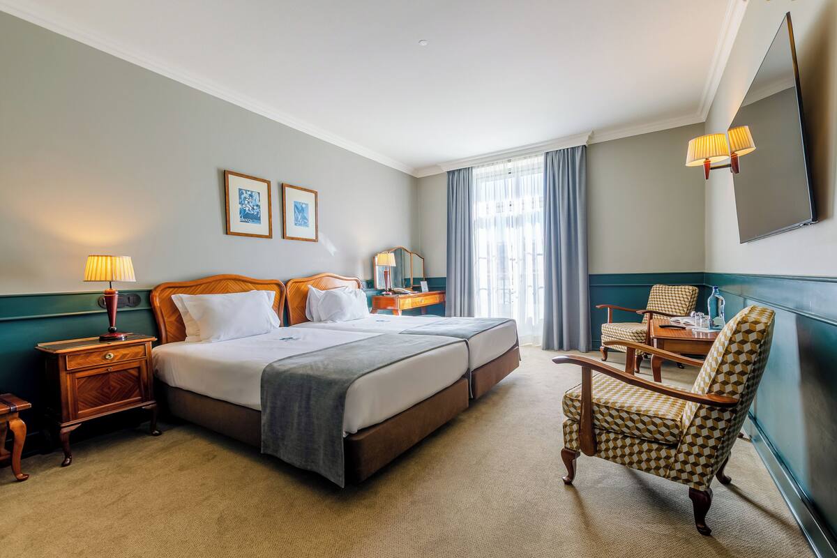 A hotel room with a double bed, two bedside tables with lamps, a chair, and a large mirror.