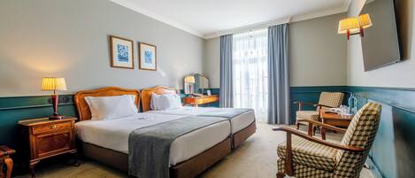 Habitación de hotel con una cama doble, dos mesitas de noche con lámparas, una silla y un espejo grande.