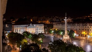 A nighttime cityscape with a prominent building featuring classical architecture and a statue monument in the foreground. - Hotel Metropole (Lisbon)