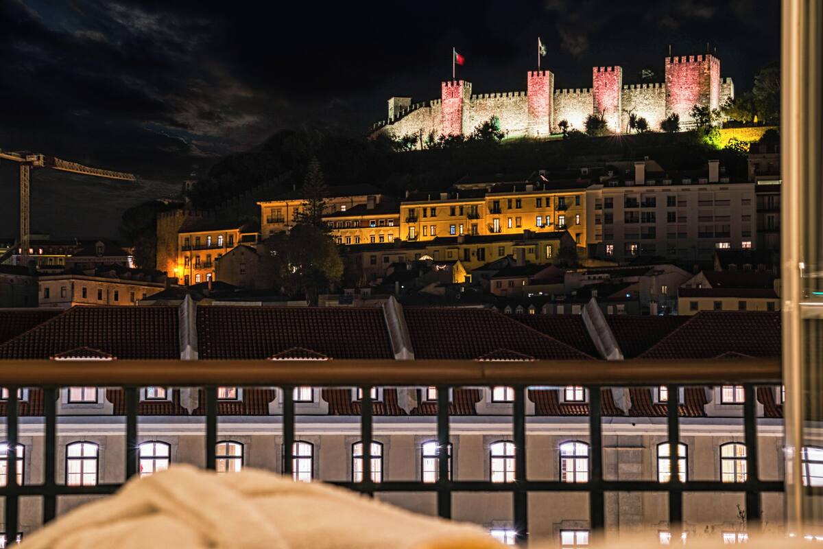 A historic castle with illuminated towers, surrounded by residential buildings with visible balconies and windows.