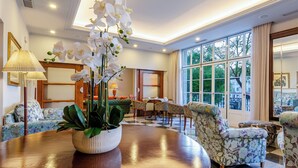 A well-lit, spacious room with a large window, a round wooden table, floral-patterned chairs, and a potted plant. - Hotel Metropole (Lisbon)