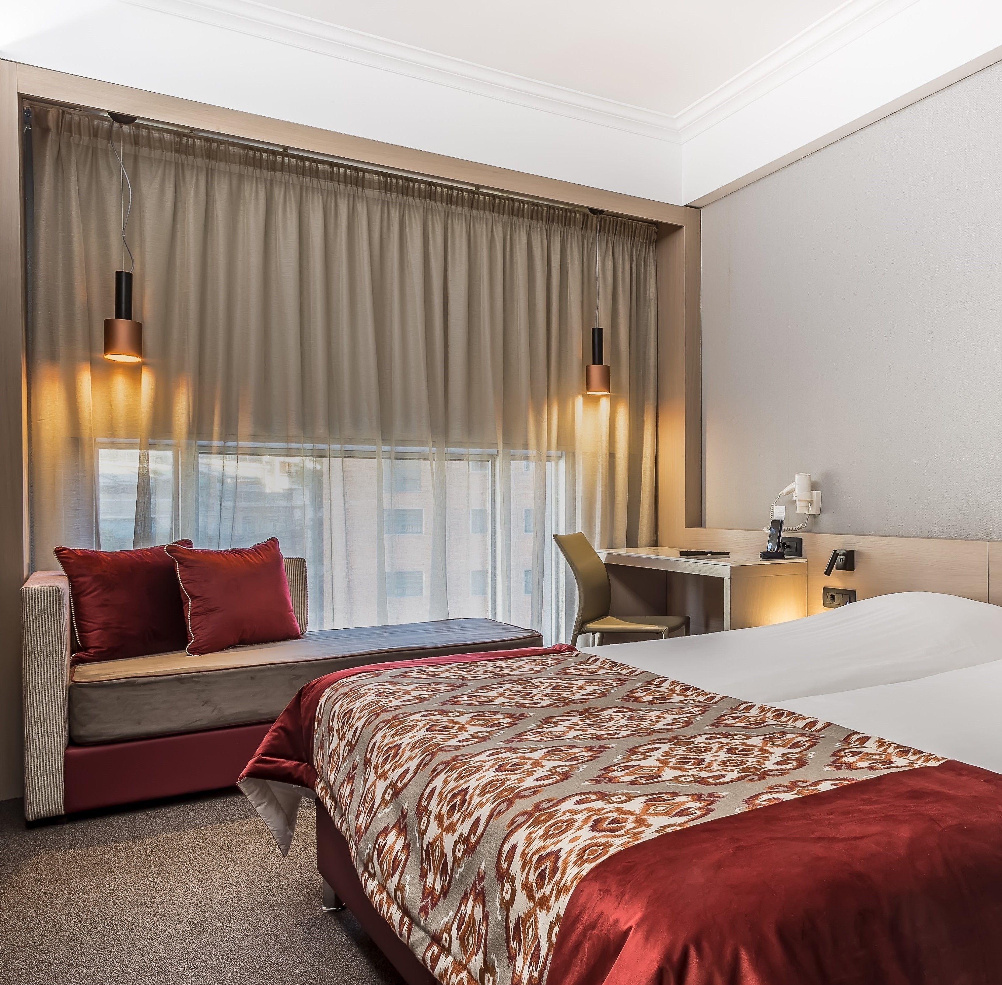 A hotel room with a large bed, a desk, a chair, a sofa, and two pendant lights.