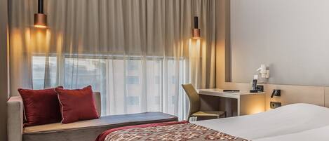 A hotel room with a large bed, a desk, a chair, a sofa, and two pendant lights.