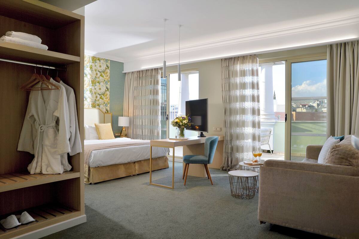 A hotel room with a bed, desk, chair, sofa, and a wardrobe.