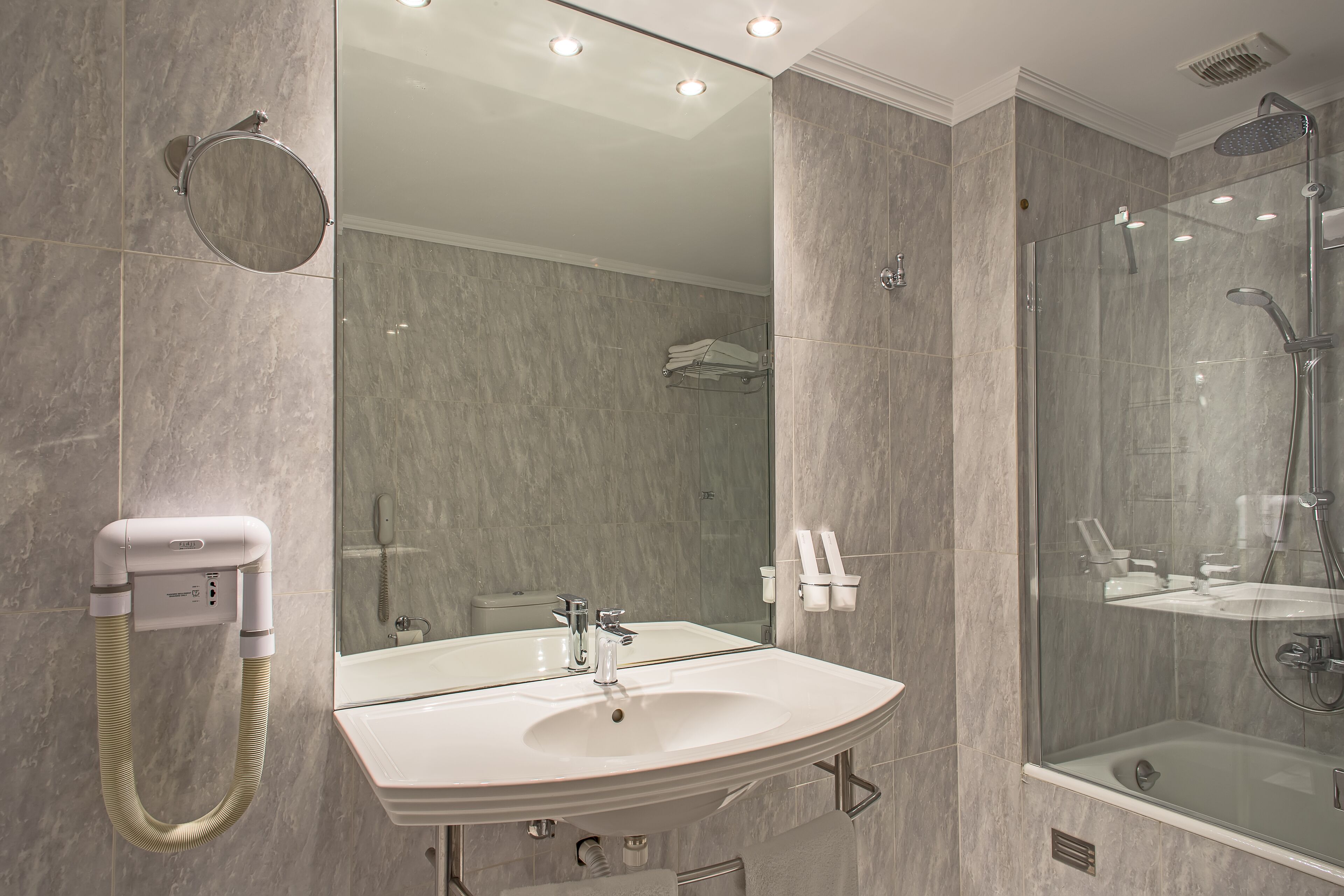 A modern bathroom with a large mirror, a sink, and a glass-enclosed shower area.
