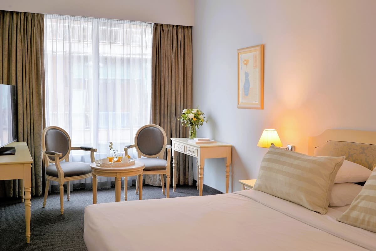 A hotel room with a bed, two chairs, a desk, a lamp, and a window with curtains.