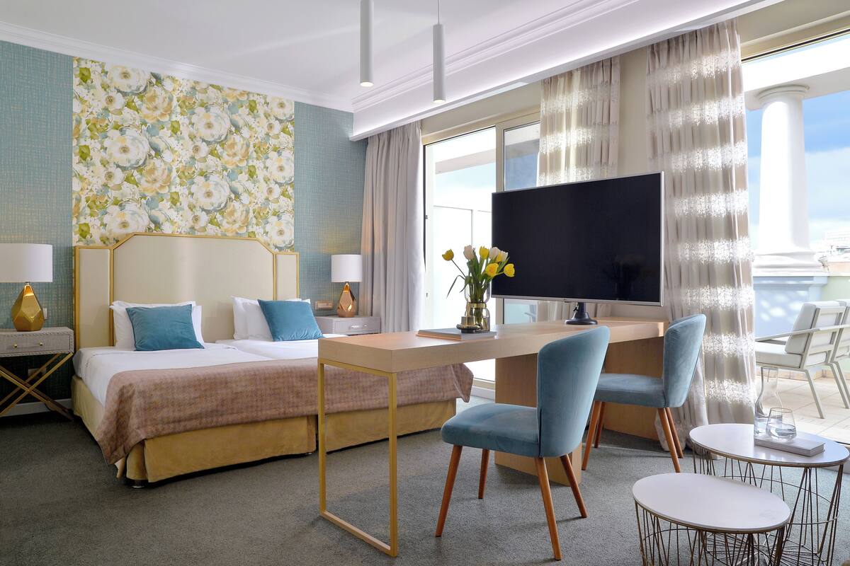 A hotel room with a bed, desk, two chairs, a TV, and a balcony with a view.