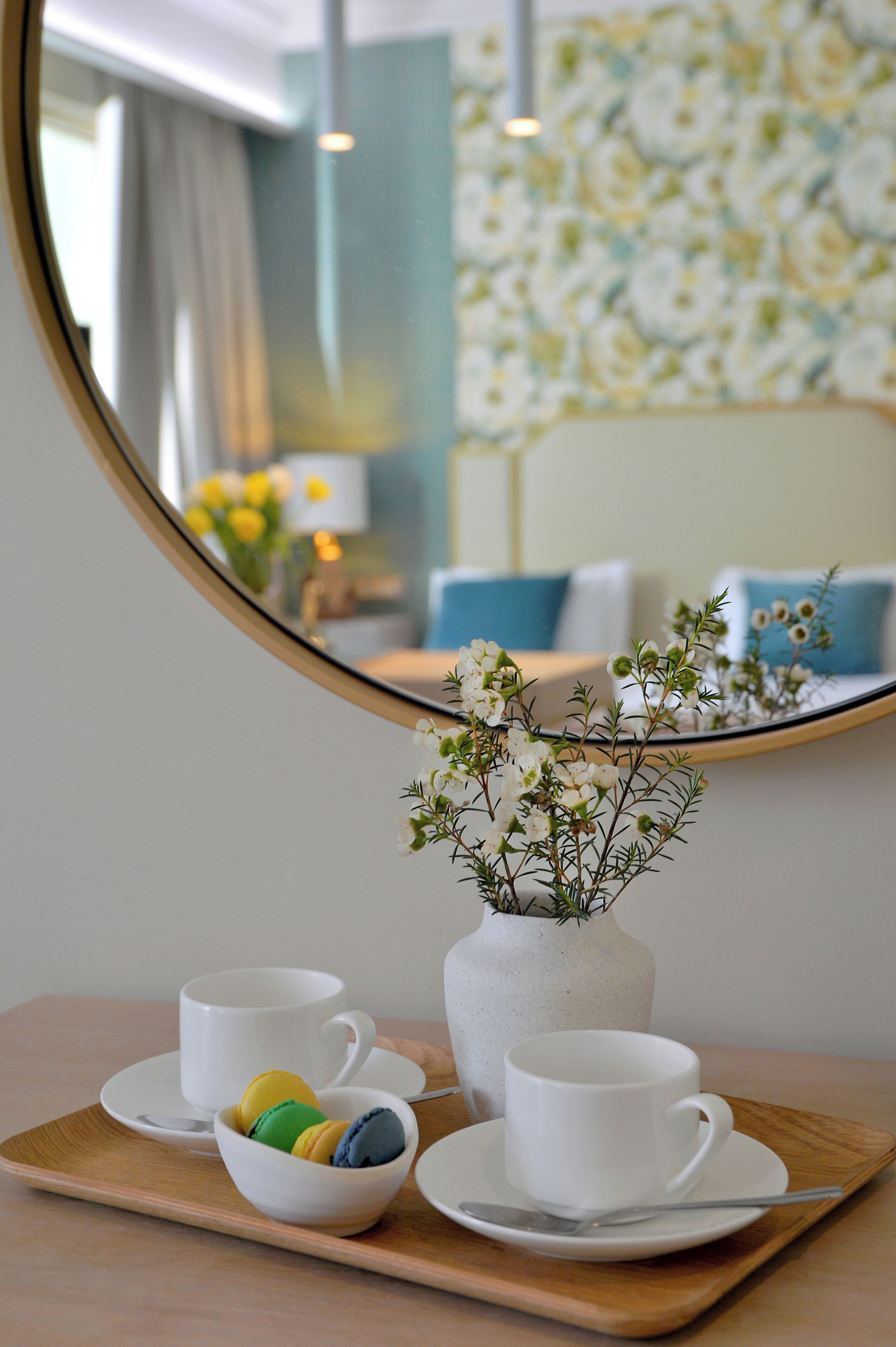A tray with a white cup, a bowl of macarons, and a white vase with flowers.